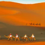 Travelers riding camels at sunset in the Sahara Desert during their morocco 10 day itinerary.