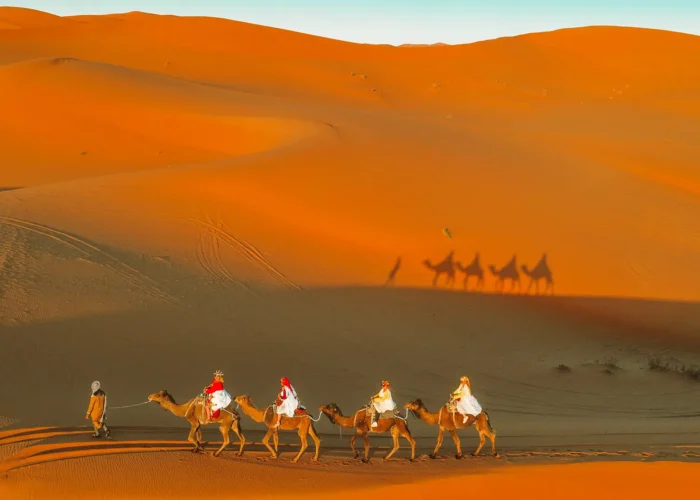 Travelers riding camels at sunset in the Sahara Desert during their morocco 10 day itinerary.